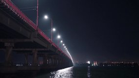 Bottom view of a beautiful bright long bridge with cold lights and fast cars over the big beautiful Dnieper river in Dnepropetrovsk in beautiful Ukraine. UHD 4K realtime video