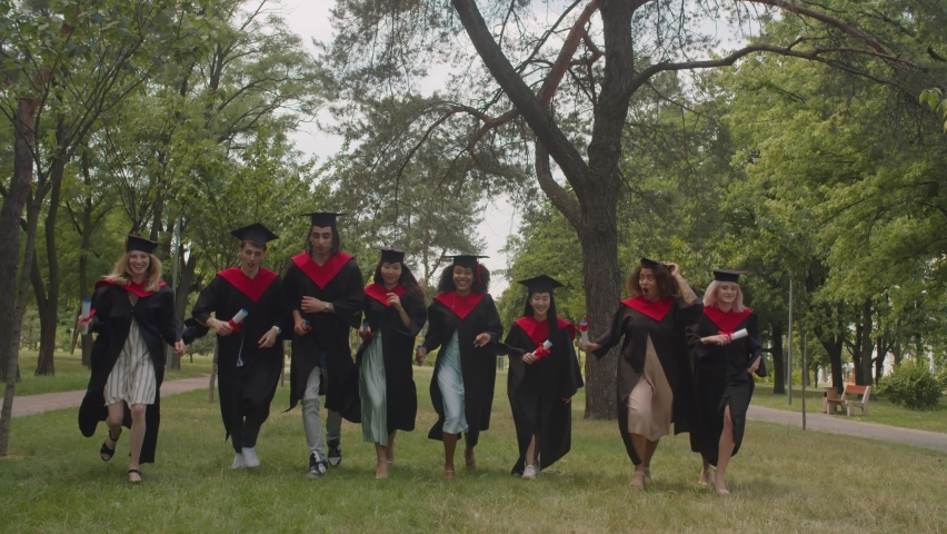 Group of carefree successful diverse multiethnic graduates with diplomas in graduation gowns and mortarboards running to cross red finish line, expressing cheerful mood and happiness outdoors. | Shutterstock HD Video #1077165302