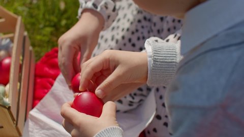 Easter holiday picnic outside. Close up of children's hands peeling red Easter eggs