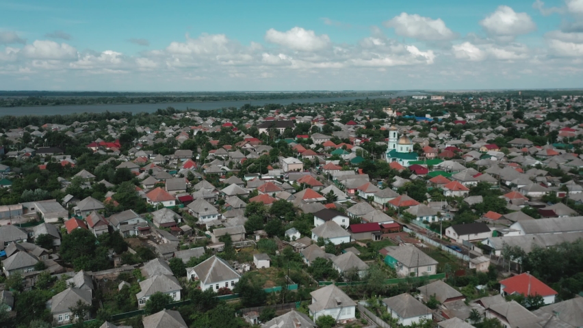 Aerial view of a large village by the river against the backdrop of a cloudy blue sky on a warm summer day. Drone view of a small town on at daytime.