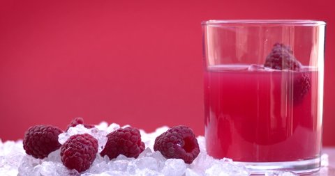 Chunks of ice fall on fresh raspberries in ice cubes, raspberry juice in a crystal glass on ice on a pink background. Natural drink and fresh fruit. Slow motion, filmed on cinema camera, 8K downscale.