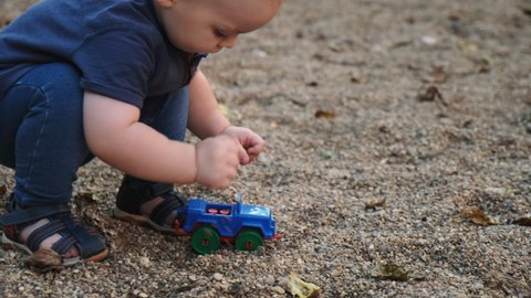 Caucasian baby boy playing with plastic toy car on playground. Childhood, baby leisure activities concept.