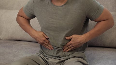 Chinese Man squeezing belly with hands because of abdominal pain. Adult guy suffering from stomach ache. Healthcare, problem with bowel flatulence concept.