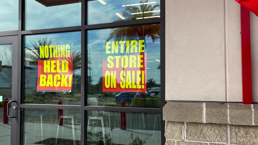 Panning right on signs in the window of a retail store going out of business that say the entire store on sale, everything must go and nothing held back.