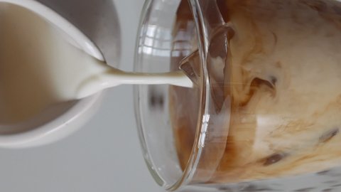 Milk cream is poured into a iced coffee. Coffee cold drink with ice and milk.vertical screen
