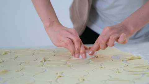 Young woman is cutting circles of dough for cooking dumplings using special form on kitchen at home, hands closeup. Process of cooking dumplings. Minced meat, dough and rolling pin on the table.