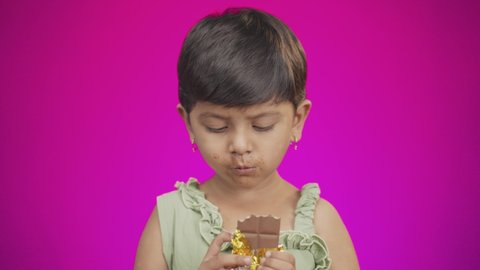medium Close up of girl kid enjoying eating chocolate on pink studio background - concept of unhealthy food consumption and child chocolate addiction.