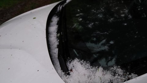 Accumulated hailstones on a car windscreen after a huge summer hailstorm. Unpredictable weather conditions, solid precipitation, climate change concept. Car damage from ice, close up panning 4k video