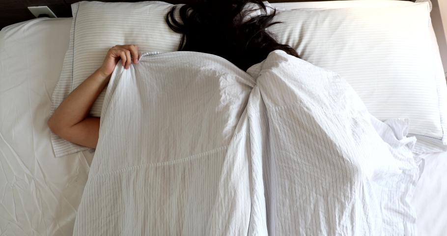 Fun loving young married couple hiding under blanket in bed, top view