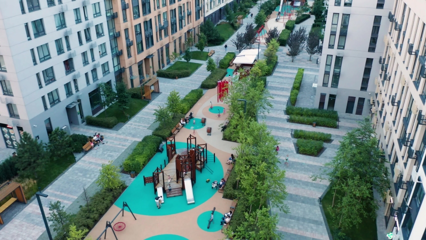 Children's playground among city streets. Children's playground surrounded by tall buildings. Modern district in the city with high-raised apartments and a playground inside. | Shutterstock HD Video #1077187841