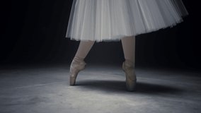 Closeup graceful ballerina legs dancing on tiptoe on dark stage. Unrecognizable dancer feet doing ballet steps in pointe shoes indoors. Unknown woman performing classical dance inside. 