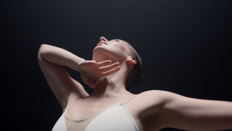Closeup graceful woman dancing in dark class. Sensual ballerina bending indoors. Female ballet dancer raising hands inside. 