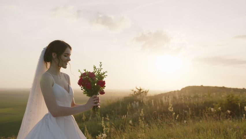 Cheerful young lady starts to smell her bunch of flowers, sunset, green plants