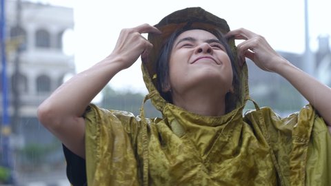 Asian girl take off raincoat hoodie to enjoy the falling rain, standing on the road side, looking up to the sky enjoying the rain drops to her face smiling, feel fresh, season climate change 