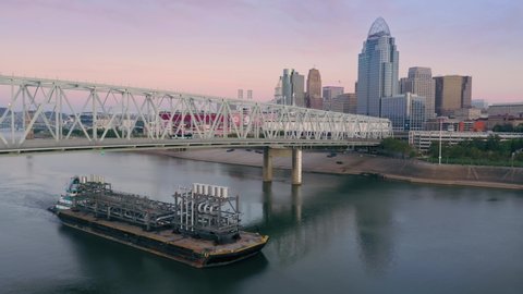 Aerial: Barge and the Purple People Bridge crossing the Ohio River. Downtown Cincinnati at sunrise, Ohio, USA. 