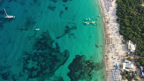 View from above, stunning aerial view of a white sand beach bathed by a turquoise water and relaxed people under some beach umbrellas at sunset. Cala di volpe beach, Costa Smeralda, Sardinia, Italy.