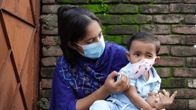A mother tries to teach her child to wear a safety mask to prevent infection. Mother and baby are clapping their hands in the joy of wearing the mask. Hygiene and safety concept. Slow-motion video.