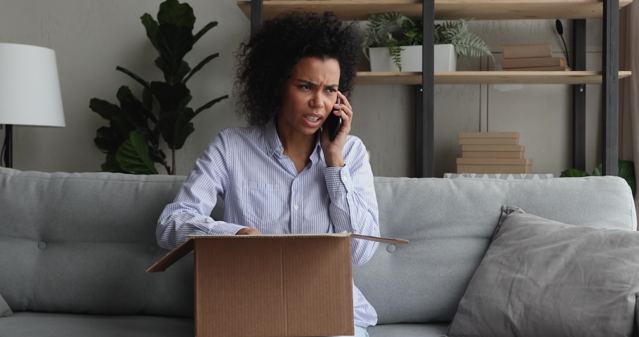 Unhappy millennial african ethnic female client feeling dissatisfied with received item, telling complaints in mobile phone call. Stressed young mixed race client having negative shopping experience. Royalty-Free Stock Footage #1077207821