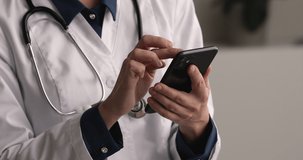 Close up young female general practitioner doctor holding smartphone in hands, using medical software applications, typing message giving distant consultation to patient or web surfing information.