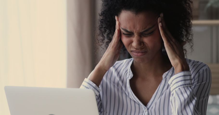 Head shot overwhelmed stressed young african american biracial woman suffering from headache, working on computer on difficult tasks. Unhappy mixed race lady feeling overworked in office room. | Shutterstock HD Video #1077207986