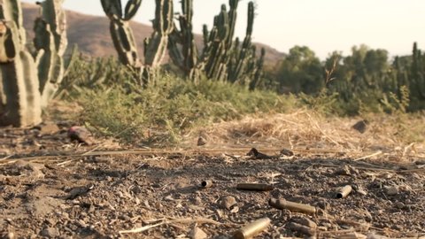 Bullet casings falling to the ground in cactus field in the desert. slow motion smoke coming out. Wild wild west cowboys scenery. Gun bullet shells flying in slow motion after being shot.