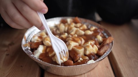 Close up of a fork taking bits from a poutine, the famous French-Canadian meal made out of fries cheese and gravy