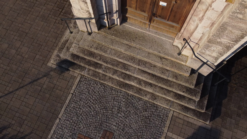 Top down rise aerial shot in front of the doors of a church in the countryside of Vionnaz, Switzerland on a sunny day.