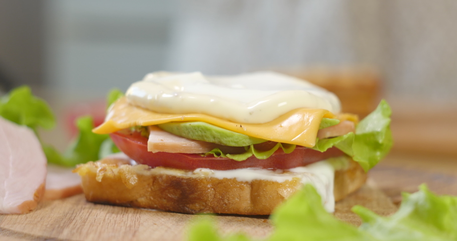 Big appetizing Sandwich with ham, ripe tomato slices and pieces of cheese, lettuce and mayonnaise sauce. Fast food concept. Ultra 4K | Shutterstock HD Video #1077226712