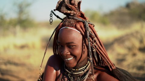 Slow motion shot of beautiful young Himba woman smiling, wearing traditional jewelry and Erembe headpiece in her village near Kamanjab, northern Namibia, Africa. 