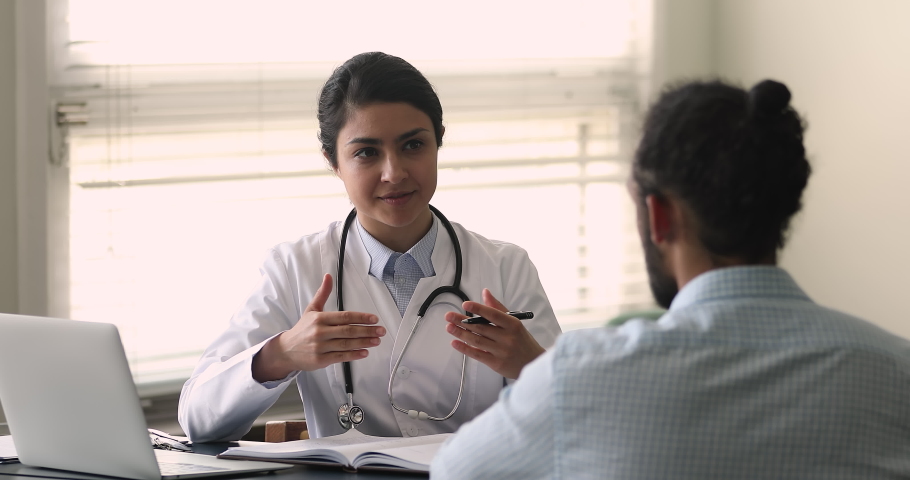 Indian woman physician talk to patient at appointment in hospital. Clinic client African man listens professional cardiologist advices, checking up health to prevent heart diseases. Healthcare concept | Shutterstock HD Video #1077230906