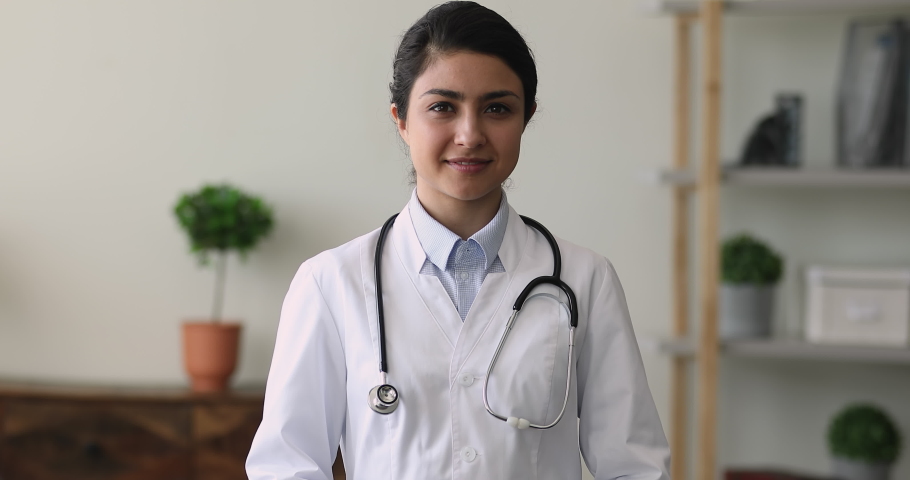 Portrait of happy Indian woman medic cardiologist in white uniform smile look at camera show love sign gesture with fingers. Cardiology, heart check up, healthcare, medical insurance, medicare concept Royalty-Free Stock Footage #1077230975