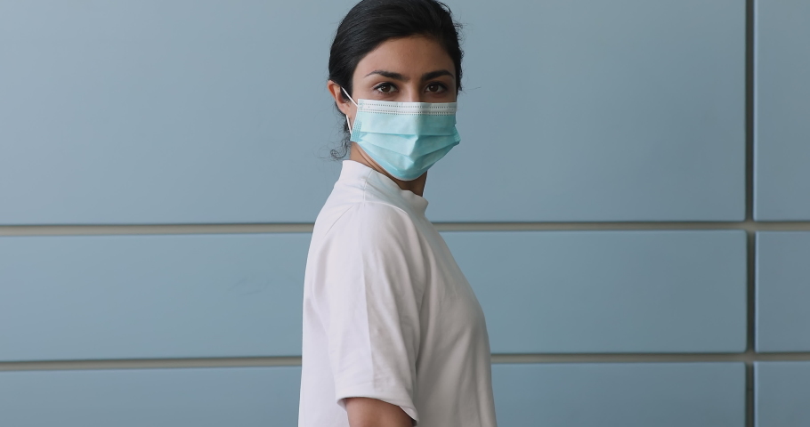 Happy young Indian female standing indoor wear protective surgical face mask showing adhesive bandage on shoulder after antivirus vaccine. Stop Covid-19 pandemic outbreak. Global vaccination concept Royalty-Free Stock Footage #1077230993