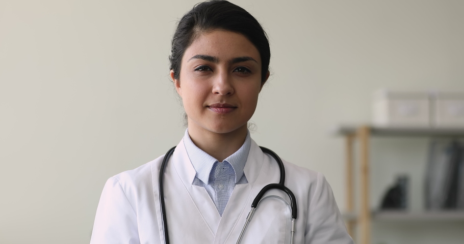 Close up young Indian female therapist wearing white coat holding piggy bank box pose in clinic office. Healthcare services expenses, health medical insurance cover, money savings and costs concept Royalty-Free Stock Footage #1077231041