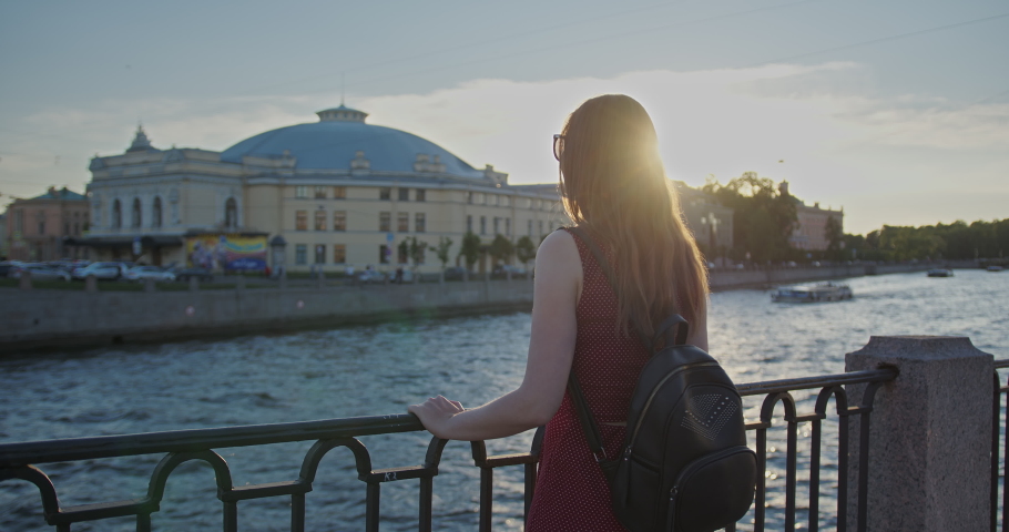 A young pretty girl in sundress walks along the river embankment on the old town