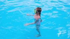 Girl somersaults and plays in the transparent blue swimming pool water. Child have fun in swim pool. Full HD slow motion video.