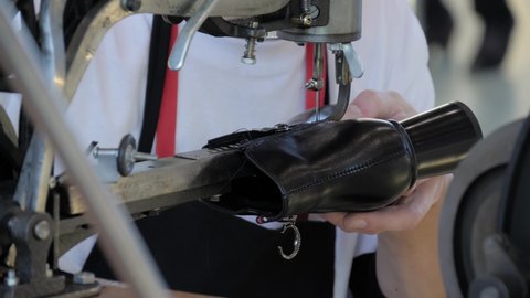 Shoemaker, shoes master using sewing machine and repairing black leather women footwear at workshop - close up
