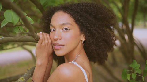 Fashion close up slow motion portrait of sensual attractive young naturally beautiful African American woman with afro hair posing in nature parkland in green foliage