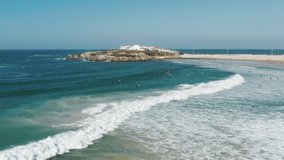Baleal, Portugal, Europe. Aerial view of idyllic beach washed with bluish ocean. People floating within foamy waves. High quality 4k footage