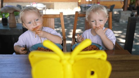 Twin sisters learning to feed themselves with their hands developing motor skills. Lunch outdoors 