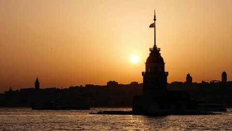 sunset in the Bosphorus Maiden's Tower and Galata Tower silhouette, the sun sets behind the Maiden's Tower. the sky in yellow and orange tones and the ferries passing Bosphorus.
