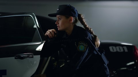 Attractive policewoman getting out of patrol car. Police officer using walkie talkie. Female cop passing information to police office. Serious woman in police uniform running after criminal 