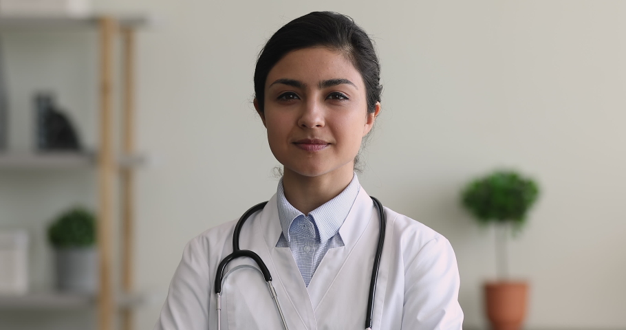 Professional medical worker, gynaecologist, paediatrician or pharmacist portrait concept. Head shot of Indian ethnicity 30s doctor wear white uniform smile look at camera while stand in clinic office Royalty-Free Stock Footage #1077245657