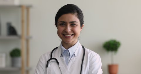 Professional medical worker, gynaecologist, paediatrician or pharmacist portrait concept. Head shot of Indian ethnicity 30s doctor wear white uniform smile look at camera while stand in clinic office