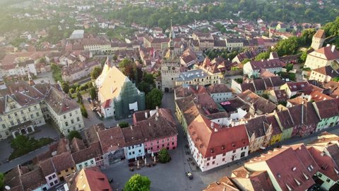 Aerial drone shot of Sighisoara, Romania. Central square with town hall and old houses with tiled roofs in Sighisoara. Warm morning light