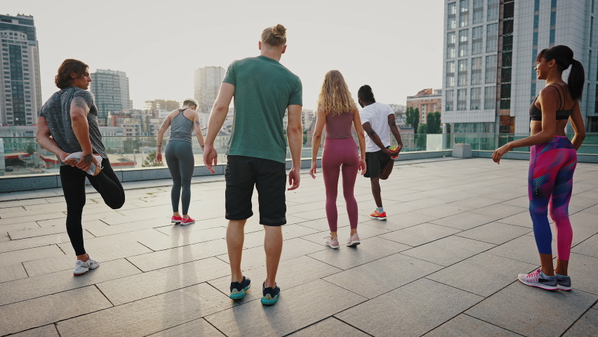 Multiracial team of young men and women, a group of like-minded people doing stretching before a morning run against the backdrop of an urban view. Girl trains a team of athletes. Royalty-Free Stock Footage #1077254735