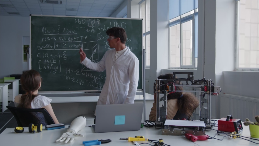 Wrote formula of 3D printer on the green blackboard, teacher in white coat and goggles