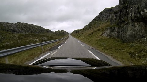 A black car driving in the Norwegian mountains in the summertime. POV shot. Action camera mounted on the top of the car. The car in focus.
