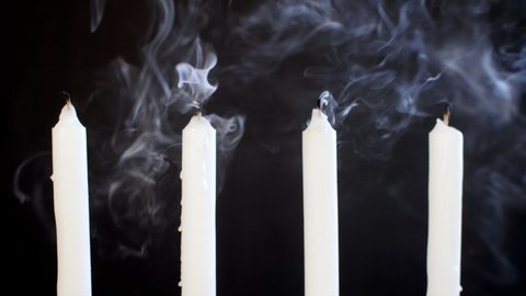 Extinct wax candle kept against a dark background - end of sorrow and sadness. Closeup shot of smoke coming out of four white candles kept against a black background