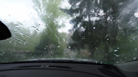 Hailstones hitting a car windscreen. Driving in bad conditions, huge summer hailstorm. Unpredictable weather conditions, solid precipitation, climate change concept. Car damage from ice, close up 4k