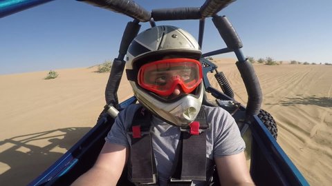 GoPro camera mounted on dune buggy to give a third person view of man in a helmet driving through the desert, past a flock of camels.